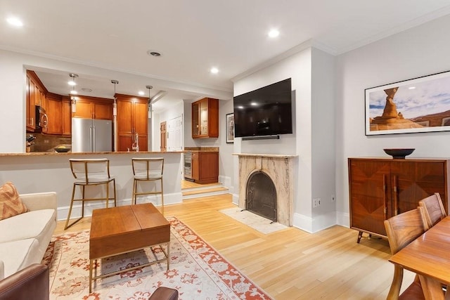 living room featuring recessed lighting, a fireplace with flush hearth, baseboards, ornamental molding, and light wood-type flooring