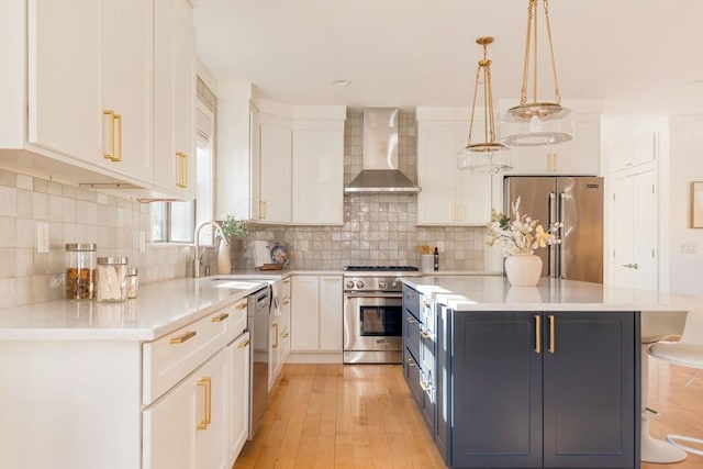 kitchen with hanging light fixtures, wall chimney exhaust hood, backsplash, white cabinetry, and high end appliances