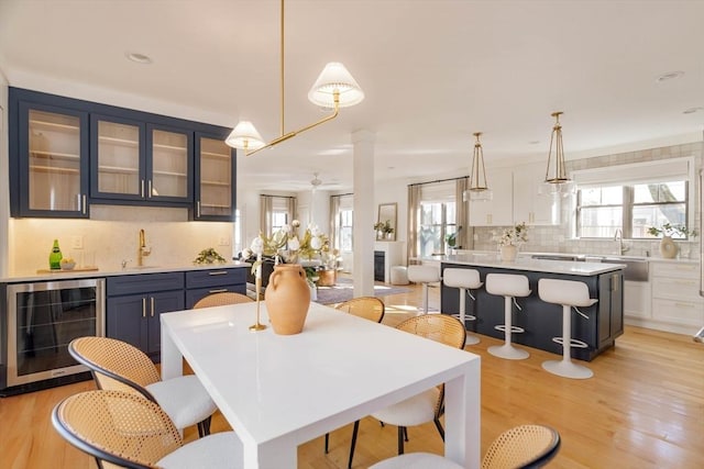 dining area with light wood-type flooring, indoor wet bar, wine cooler, and ceiling fan