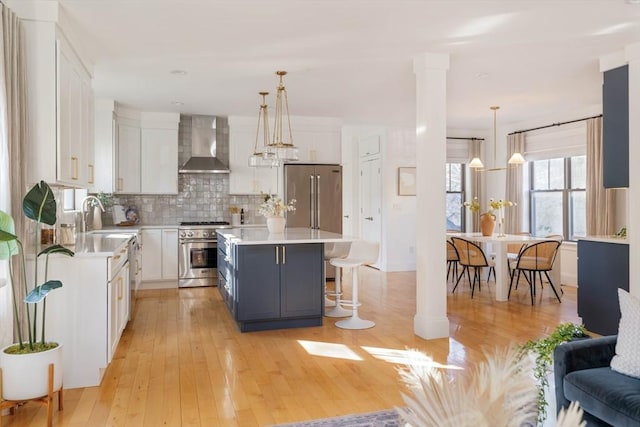 kitchen featuring white cabinets, a center island, wall chimney range hood, high end appliances, and hanging light fixtures