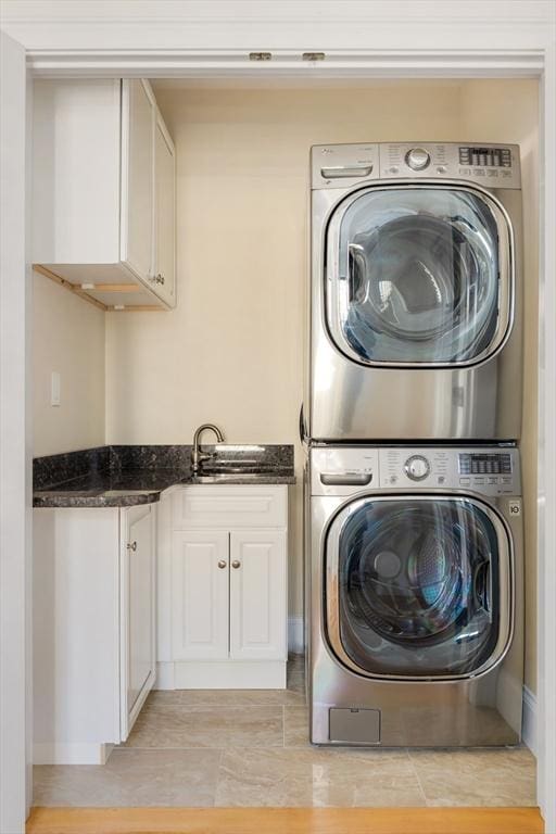 laundry room featuring sink, stacked washer / drying machine, cabinets, and light tile patterned flooring