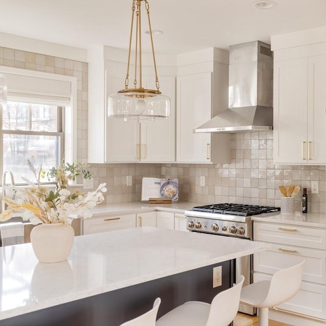 kitchen with white cabinetry, decorative backsplash, a kitchen breakfast bar, wall chimney exhaust hood, and high end stove