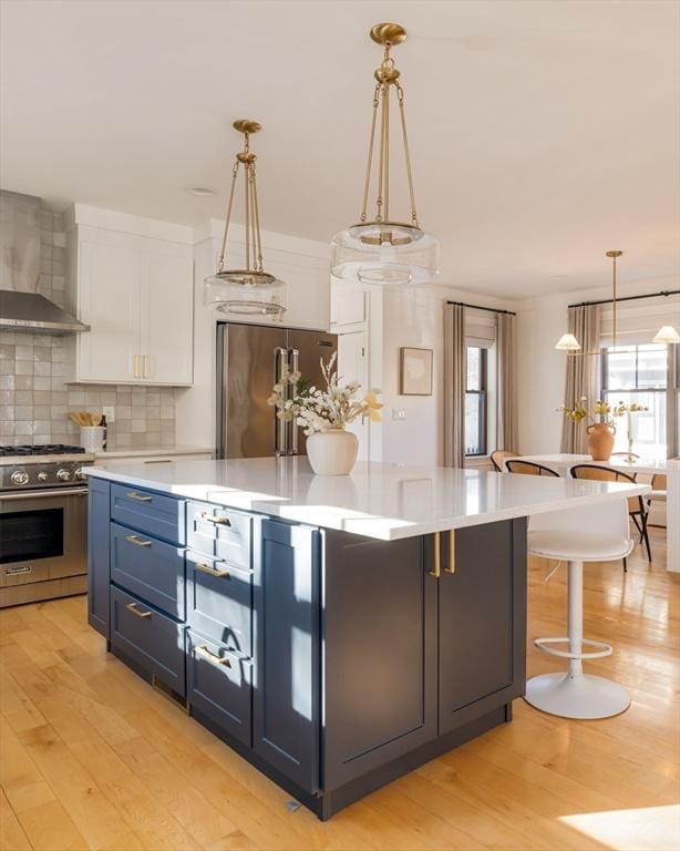 kitchen with premium appliances, white cabinets, pendant lighting, decorative backsplash, and blue cabinets