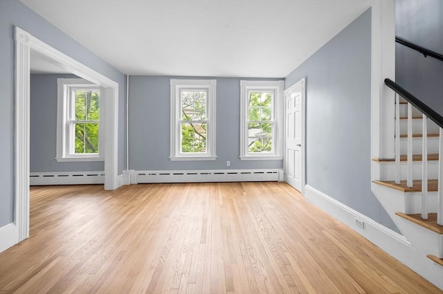 unfurnished living room with baseboard heating, light wood-style floors, stairway, and baseboards