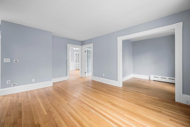 empty room featuring a baseboard heating unit, baseboards, and light wood-type flooring