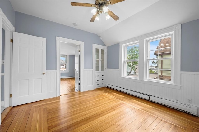 unfurnished bedroom featuring a baseboard heating unit, wainscoting, lofted ceiling, multiple windows, and hardwood / wood-style flooring