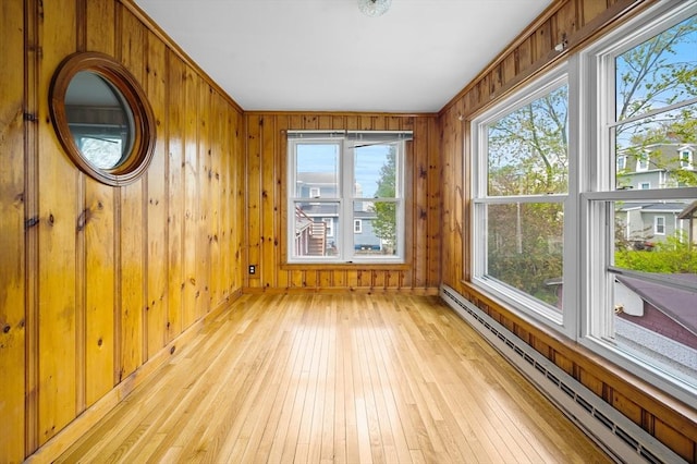 unfurnished room with a baseboard radiator, healthy amount of natural light, light wood finished floors, and wooden walls