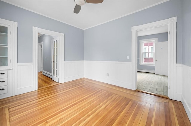 unfurnished room featuring a ceiling fan, wainscoting, wood finished floors, a baseboard heating unit, and ornamental molding