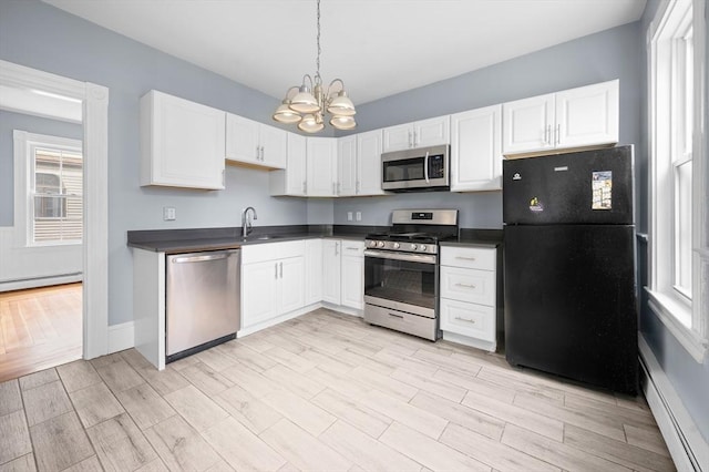 kitchen with appliances with stainless steel finishes, dark countertops, a chandelier, light wood-type flooring, and white cabinets
