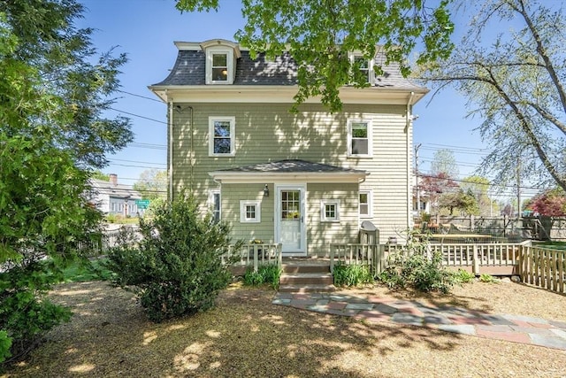 victorian home with roof with shingles, fence, and mansard roof