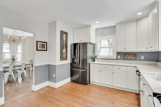 kitchen with light stone countertops, a chandelier, light wood-style floors, stainless steel appliances, and white cabinets