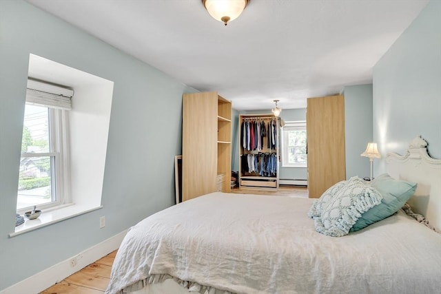 bedroom with a baseboard heating unit, baseboards, and wood finished floors