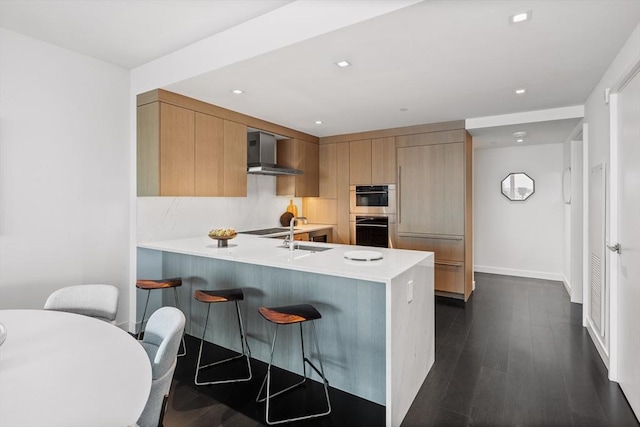 150 Seaport Blvd Unit 11C, Boston, MA 02210 - kitchen with wall chimney range hood, a peninsula, light countertops, a breakfast bar, and recessed lighting