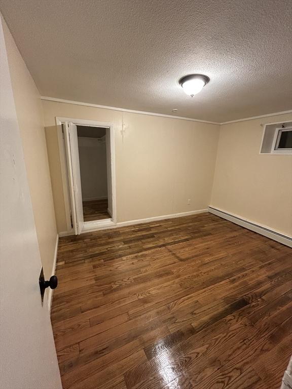 spare room featuring a textured ceiling, dark hardwood / wood-style floors, a wall mounted AC, and a baseboard heating unit