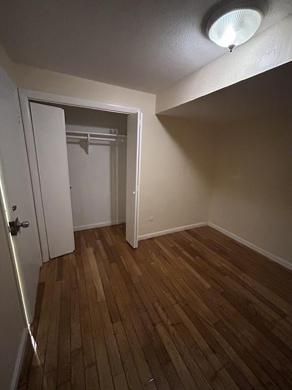 unfurnished bedroom with a textured ceiling, dark hardwood / wood-style floors, and a closet