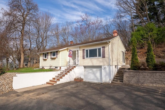 view of front of home featuring a garage, stairs, driveway, and a chimney