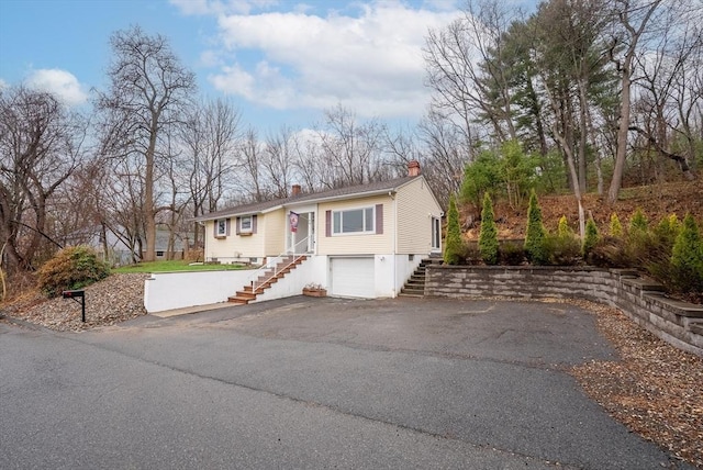 raised ranch with a chimney, aphalt driveway, a garage, and stairway