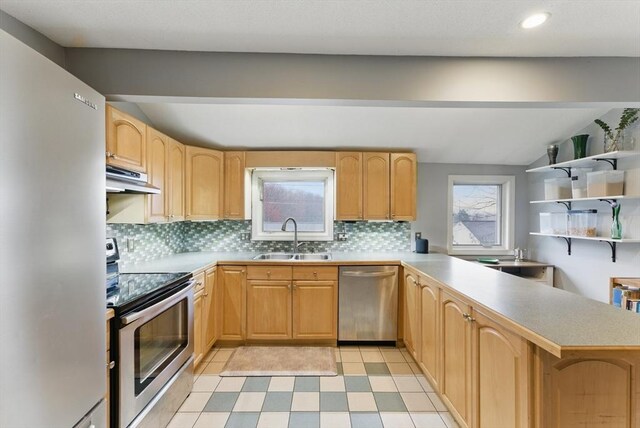 kitchen featuring light countertops, backsplash, under cabinet range hood, appliances with stainless steel finishes, and a sink