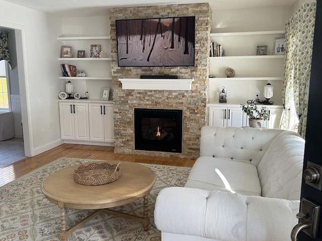 living room featuring built in features, a fireplace, and light hardwood / wood-style floors