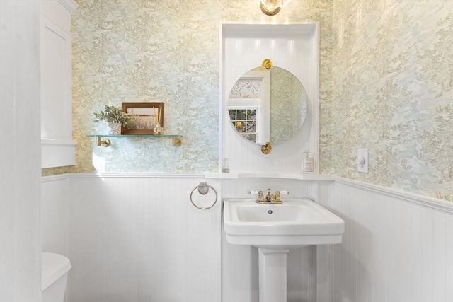 bathroom with a wainscoted wall, toilet, and wallpapered walls