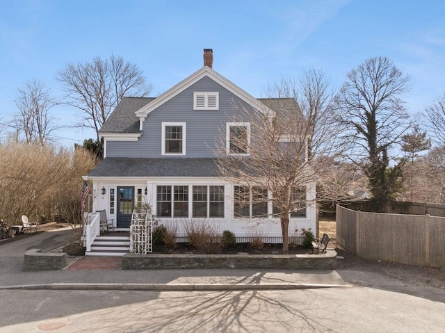 view of front of property with a shingled roof, a chimney, and fence