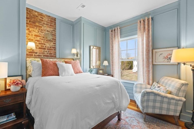 bedroom featuring brick wall and wood finished floors