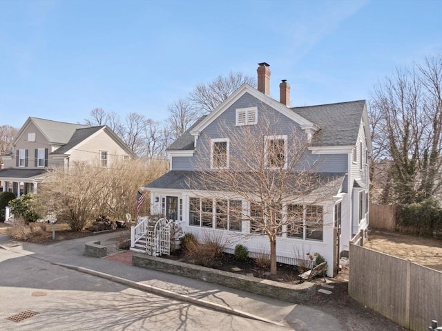 view of front of property featuring a shingled roof, a chimney, and fence