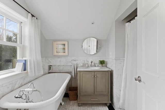 full bathroom featuring vanity, a wainscoted wall, lofted ceiling, a freestanding bath, and tile walls