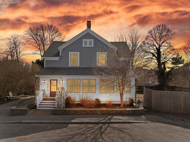 view of front of home featuring a shingled roof, fence, and a chimney