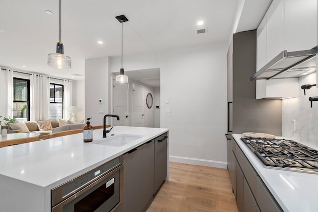 kitchen with light wood-type flooring, sink, pendant lighting, white cabinetry, and stainless steel gas stovetop