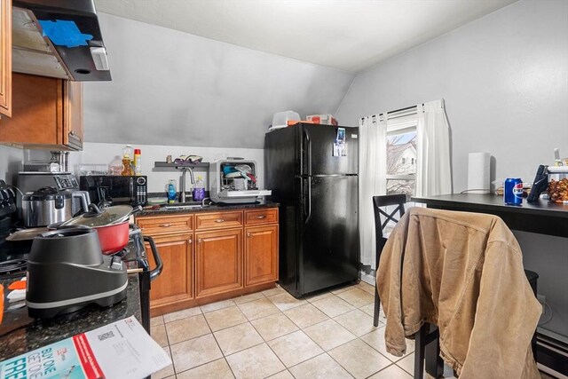 kitchen featuring light tile patterned floors, a sink, vaulted ceiling, brown cabinets, and black appliances