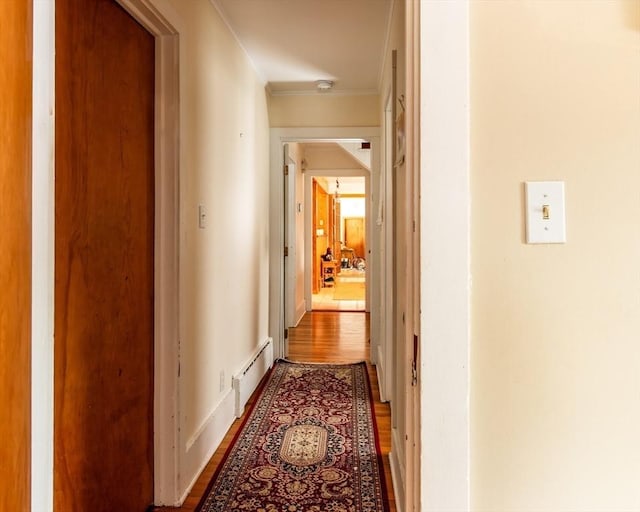 hallway featuring a baseboard heating unit, baseboards, wood finished floors, and crown molding