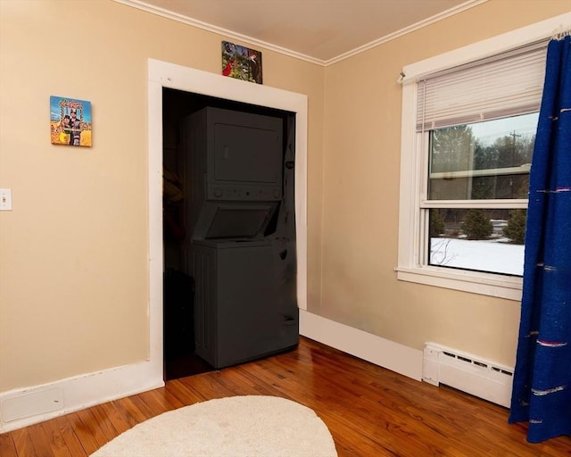 clothes washing area featuring a baseboard radiator, ornamental molding, wood finished floors, and stacked washer and clothes dryer