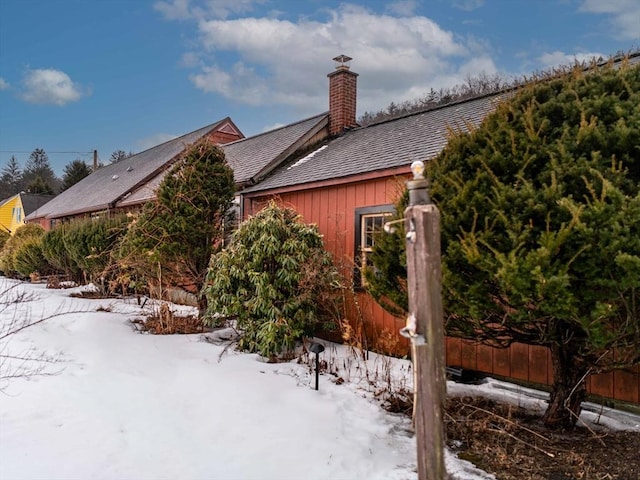 view of snowy exterior with board and batten siding, fence, a chimney, and a shingled roof