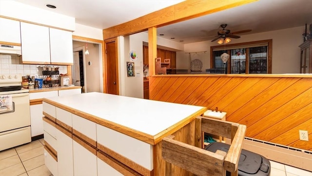 kitchen featuring white electric stove, light tile patterned floors, under cabinet range hood, white cabinets, and tasteful backsplash