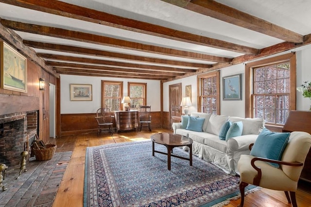 living area featuring beam ceiling, a wainscoted wall, a brick fireplace, wooden walls, and hardwood / wood-style flooring