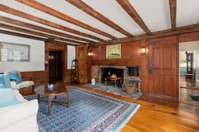 living area featuring a fireplace, visible vents, wooden walls, light wood-type flooring, and beamed ceiling