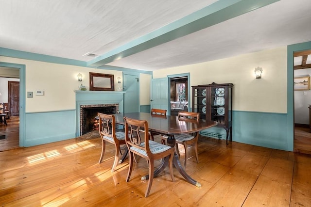 dining room with a brick fireplace, a wainscoted wall, visible vents, and light wood finished floors