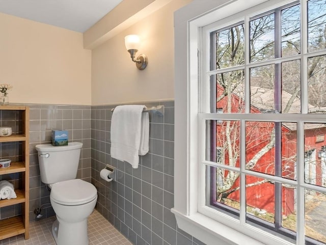 bathroom featuring toilet, a wainscoted wall, tile patterned flooring, and tile walls