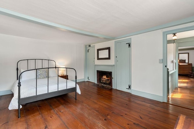 bedroom featuring a fireplace with flush hearth, baseboards, and hardwood / wood-style flooring