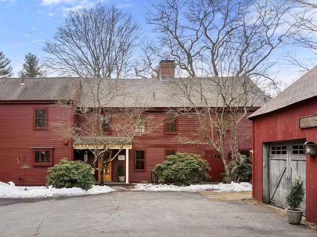 view of front facade featuring a shingled roof, a chimney, and an outbuilding