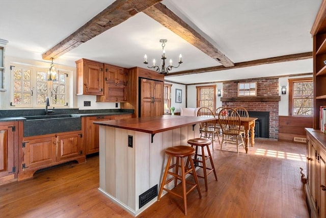 kitchen featuring light wood-style flooring, wood counters, a brick fireplace, beam ceiling, and a kitchen bar