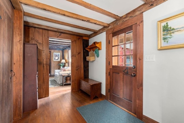 interior space featuring wooden walls, hardwood / wood-style floors, beam ceiling, and baseboards