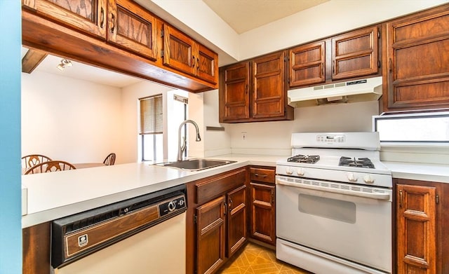 kitchen with white appliances, a peninsula, light countertops, under cabinet range hood, and a sink