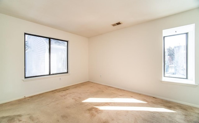 carpeted empty room with a healthy amount of sunlight, visible vents, and baseboards