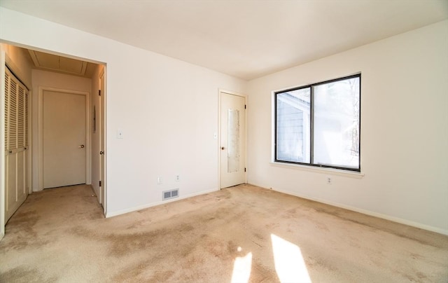 carpeted empty room featuring visible vents, attic access, and baseboards