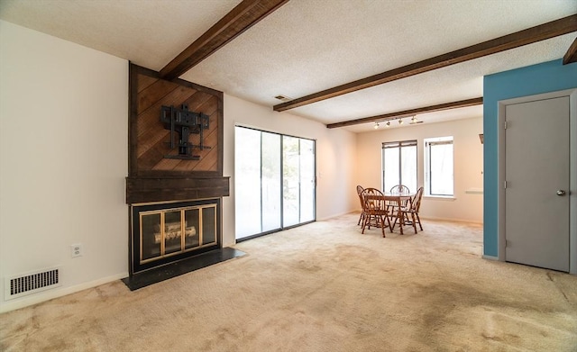 unfurnished living room featuring a large fireplace, visible vents, carpet, a textured ceiling, and beam ceiling