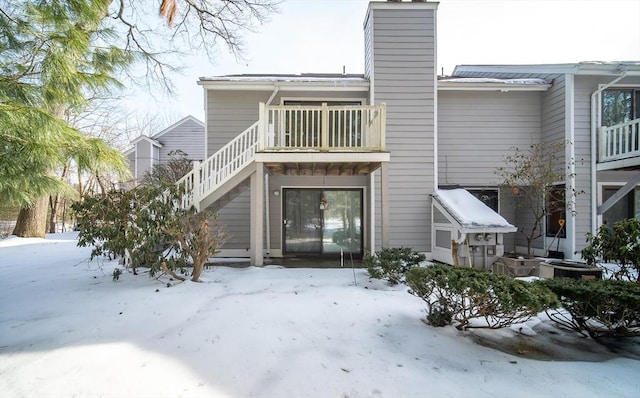 snow covered rear of property with a chimney and a balcony