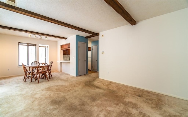 dining room with beam ceiling, light colored carpet, a textured ceiling, and baseboards