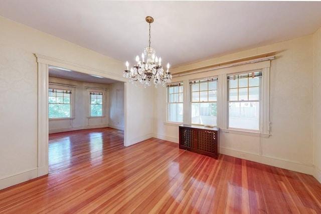 empty room featuring baseboards, a notable chandelier, wood finished floors, and radiator